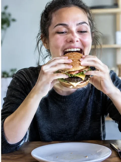 Same woman taking a big bite of the burger